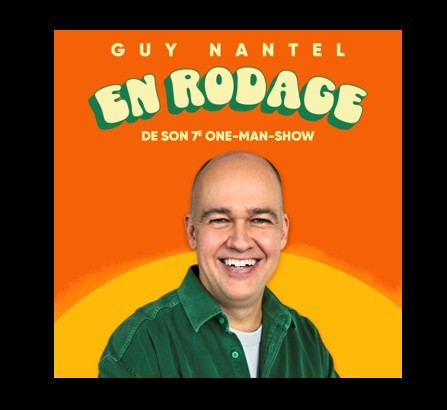 Un homme en chemise verte sourit devant un fond orange. Au-dessus de lui, on peut lire "Guy Nantel En Rodage de son 7e one-man-show" en caractères gras, ludiques, jaunes et verts.